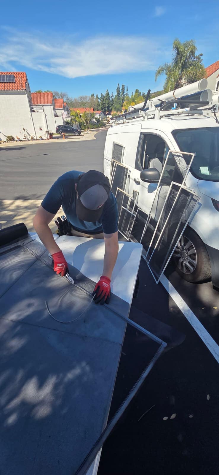 Window Screens Repair technician cutting new mesh on the tailgate beside the service van, with finished screens leaning against it, in East County San Diego