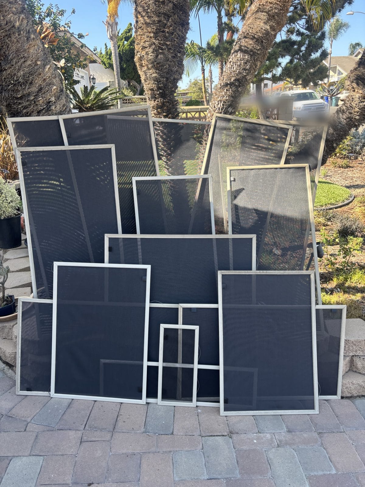 About fourteen finished solar sun screens with new mesh, lined up in an Imperial Beach driveway after a whole-house re-screen by Window Screens Repair