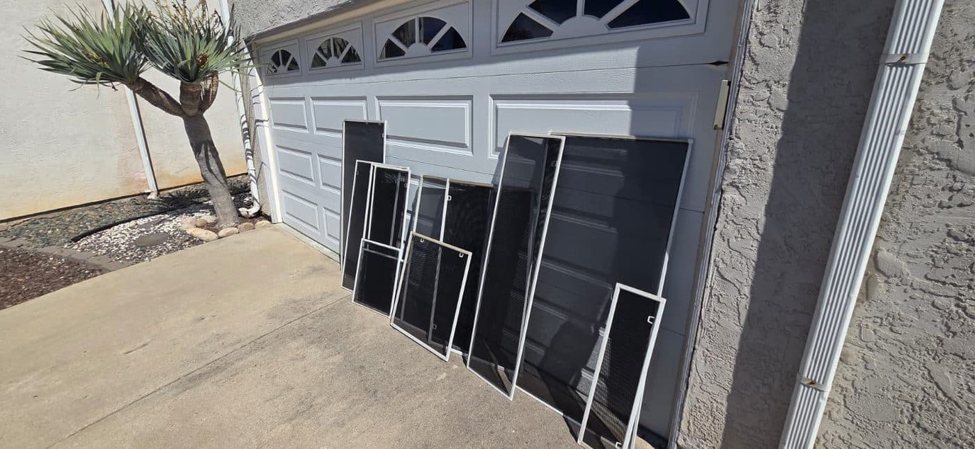 A full set of finished window screens leaning against a garage door at a Santee home