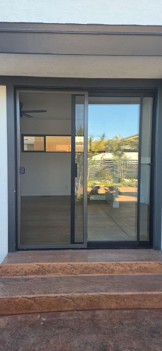 A sliding screen door fitted to a dark-framed patio slider at a Chula Vista home, looking through to the courtyard