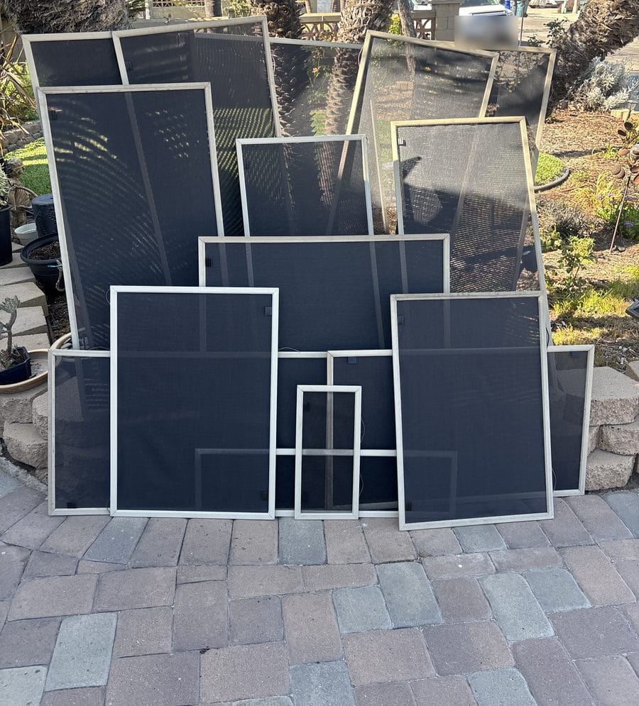 A full set of finished solar sun screens with dark charcoal mesh leaning against a garden wall before installation on a San Diego home